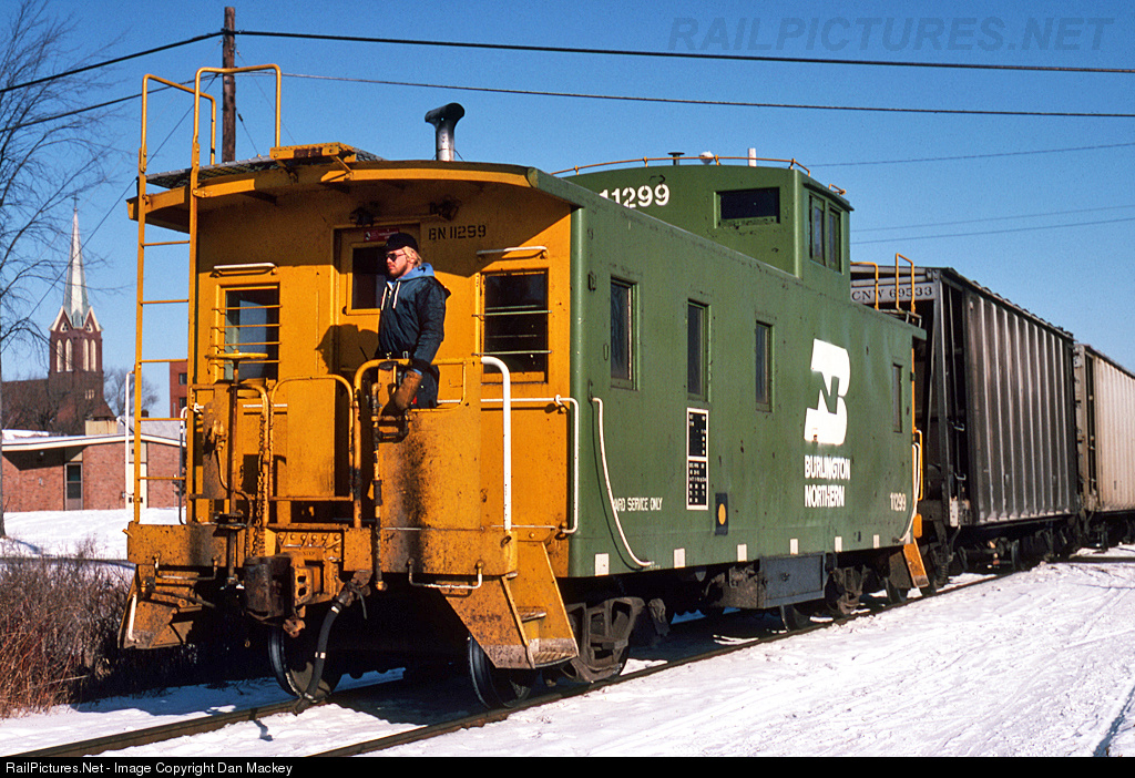 Here’s a modern caboose with an offset cupola with the cupola on the forward side – BN #11299. Pic was taken at Superior, WI, 1981. You can see the marker light mounting clips on the sides of the caboose, but I don’t see any marker lights or equivalent. Weatherers note the wheel spray marks – not sure if they are worse than normal because of winter (??).